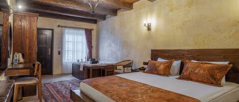 A bedroom with a wooden ceiling, a large bed with pillows, a desk, and a chair.