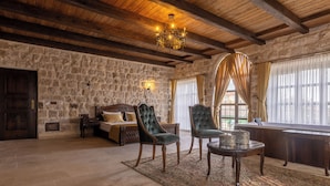 A room with stone walls, a wooden ceiling, a bed, two upholstered chairs, a small table, and a window with curtains. - Noble Blue Cappadocia  (Urgup)