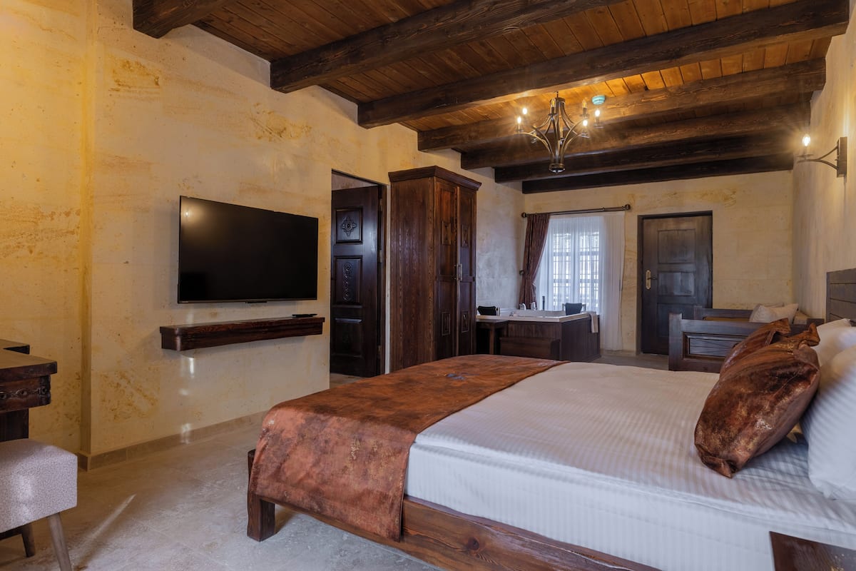 A bedroom with a bed, a TV, wooden furniture, and a chandelier.