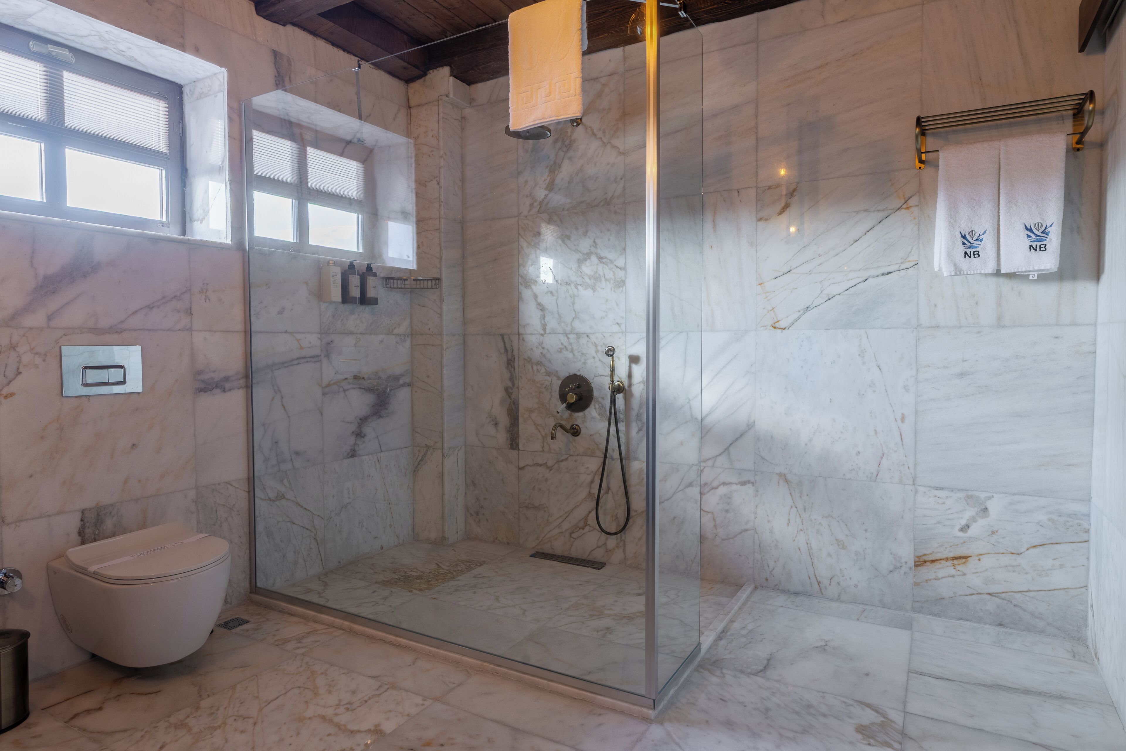 A modern bathroom with a glass-enclosed shower, a toilet, and marble walls.