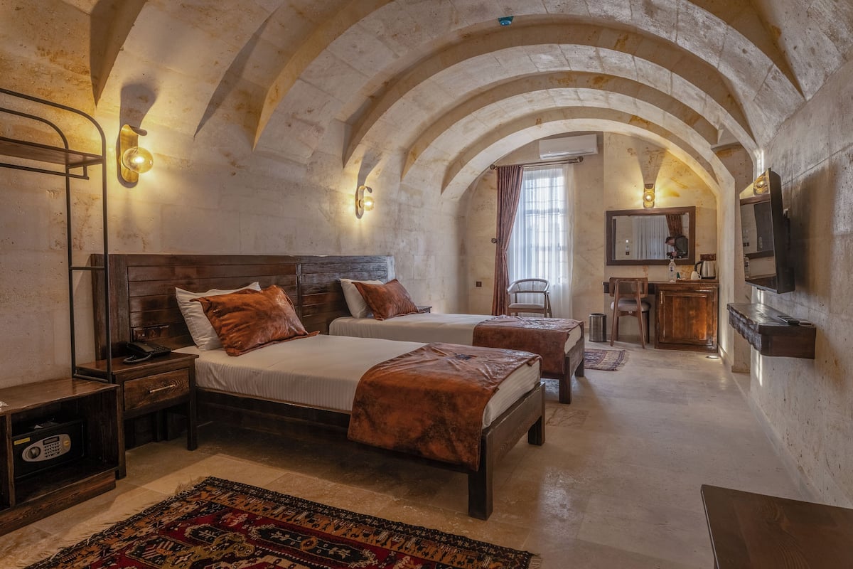 A bedroom with two beds, a wooden nightstand, a desk, a chair, and a small table.