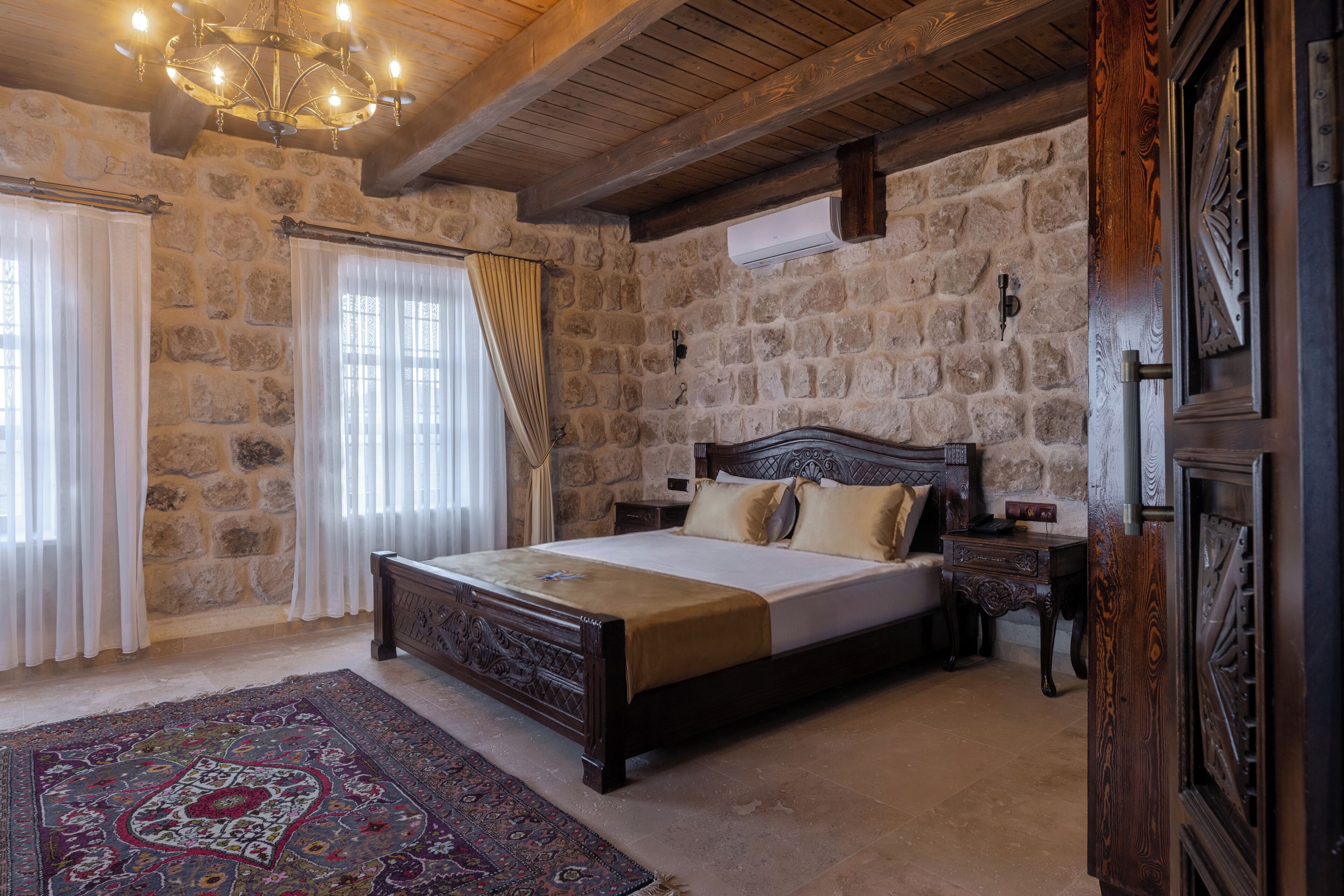 Un dormitorio con pared de piedra, estructura de cama de madera, candelabro y alfombra grande.