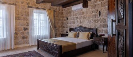 Un dormitorio con pared de piedra, estructura de cama de madera, candelabro y alfombra grande.