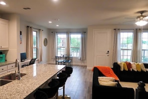 A modern kitchen with granite countertops, a dining area with a table and chairs, and a living area with a sofa and a ceiling fan.
