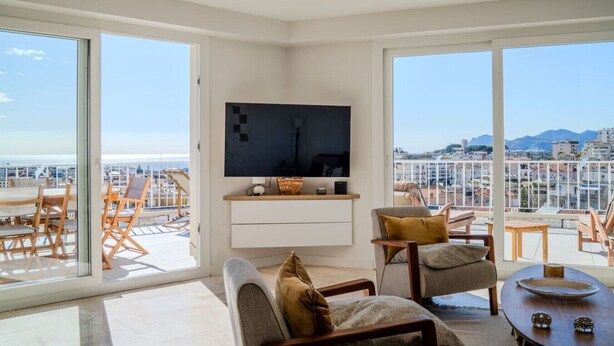 Ein modernes Wohnzimmer mit einem Flachbildfernseher, bequemen Sitzmöglichkeiten und großen Fenstern mit Blick auf die Stadt.