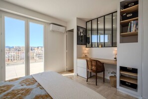 Ein Schlafzimmer mit einem Bett, einem Schreibtisch, einem Stuhl, einem Bücherregal und einem großen Fenster mit Blick auf die Stadt.