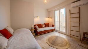 Ein Schlafzimmer mit einem Bett, einem Schlafsofa, einem kleinen Tisch, einer Lampe, einem großen Fenster und einer Leiter.