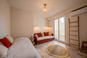 Ein Schlafzimmer mit einem Bett, einem Schlafsofa, einem kleinen Tisch, einer Lampe, einem großen Fenster und einer Leiter.