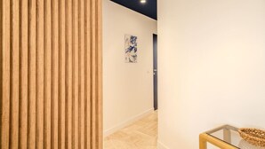 Ein Korridor mit Holzwandverkleidung, einem Glastisch mit einem gewebten Korb und einem blauen, abstrakten Gemälde an der Wand.