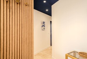 Ein Korridor mit Holzwandverkleidung, einem Glastisch mit einem gewebten Korb und einem blauen, abstrakten Gemälde an der Wand.