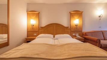 Un lit double avec une couverture beige, une tête de lit en bois, des lampes de chevet, une table de chevet avec un téléphone et un fauteuil à rayures.