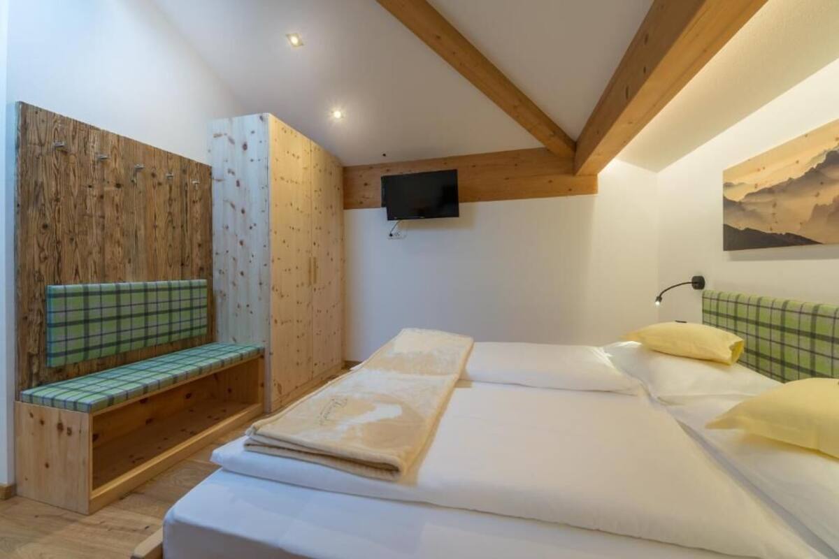 Ein Zimmer mit einem Bett, einer Bank, einem Fernseher und einem Bild an der Wand.