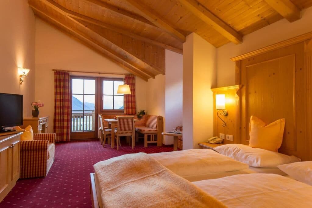 A hotel room with two beds, a desk, a chair, a TV, and a balcony with a view.