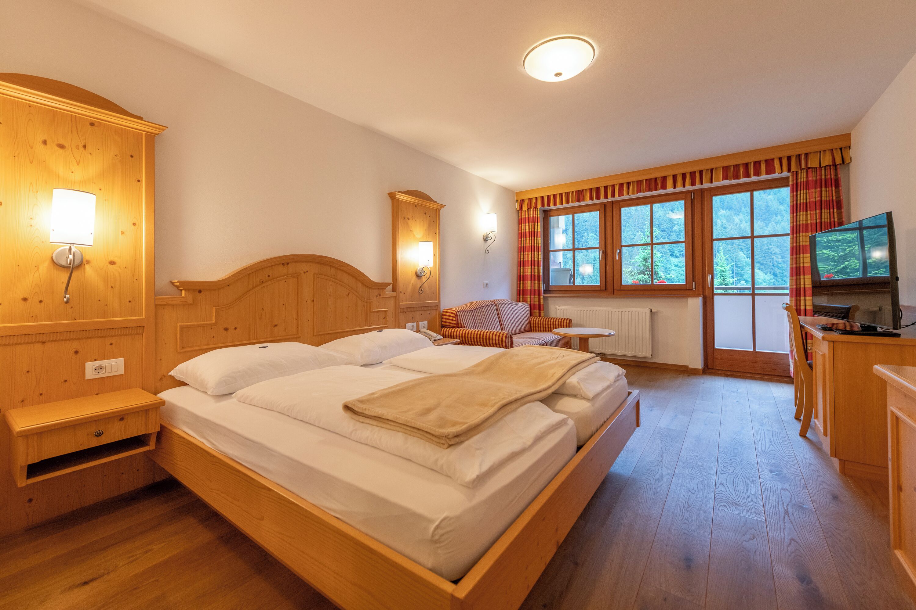 Uma cama de madeira com duas almofadas e um cobertor, uma mesa de cabeceira de madeira, um guarda-roupa de madeira, uma cômoda de madeira, uma televisão e uma janela com cortinas.