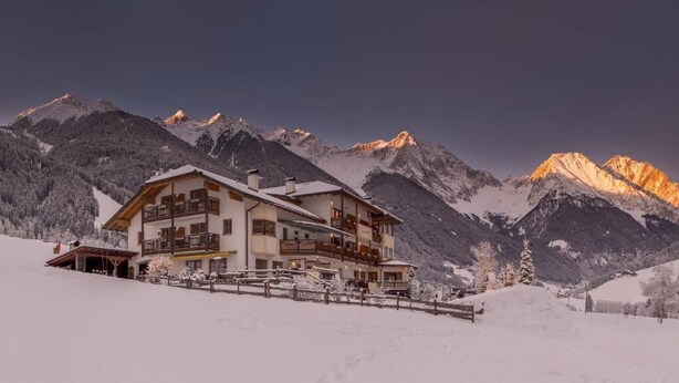 Ein mehrstöckiges Chalet mit Balkonen vor einer verschneiten Bergkulisse.