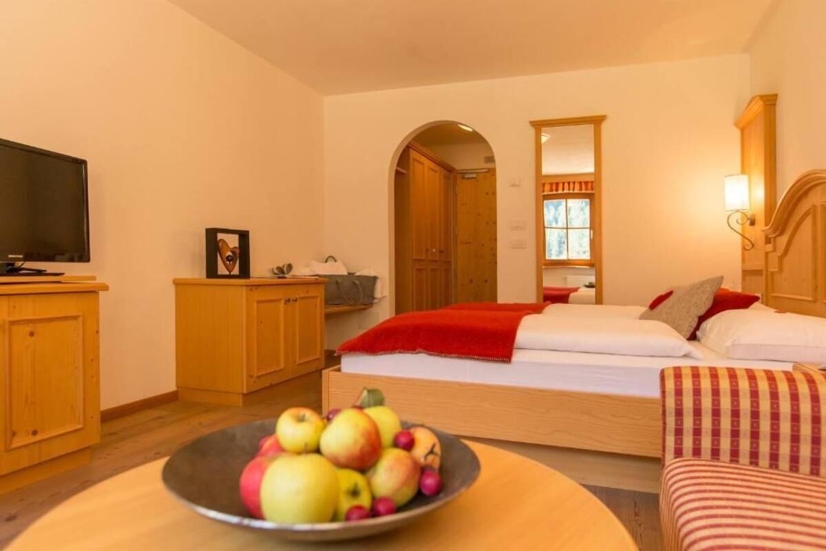 Ein Hotelzimmer mit einem Bett, einem Fernseher, Holzschränken, einer Obstschale und einem Fenster mit Vorhängen.