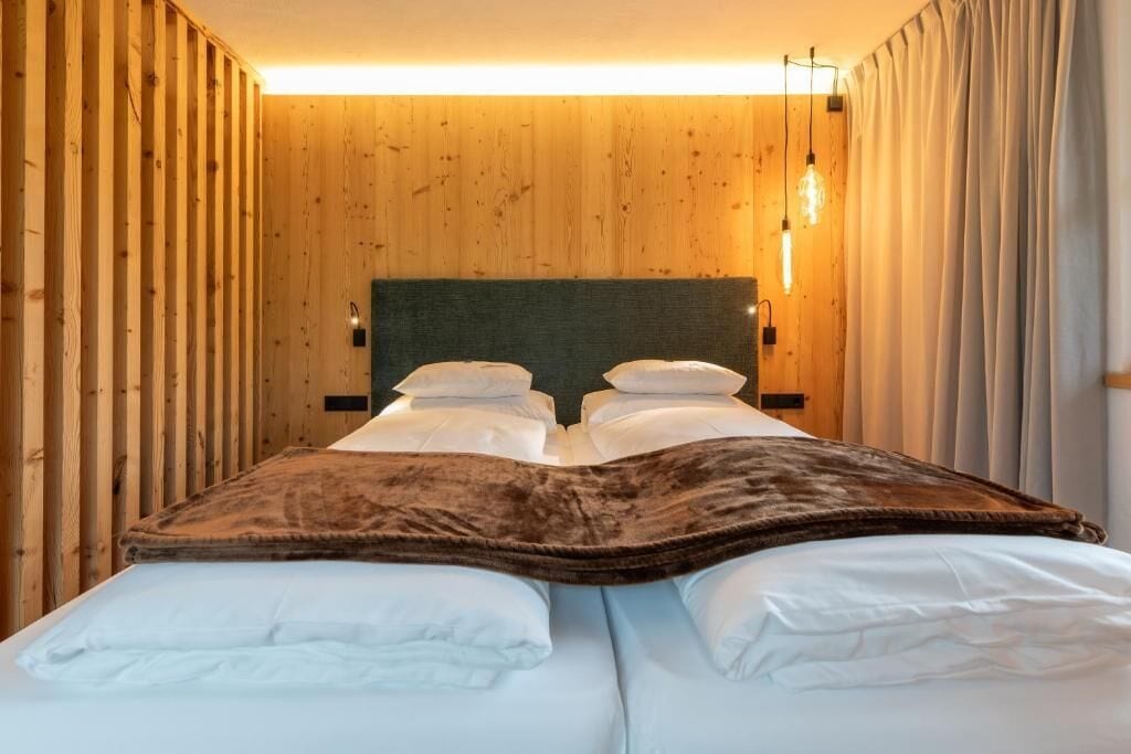 A room with a wooden wall, a bed with white bedding, and a light fixture above the bed.