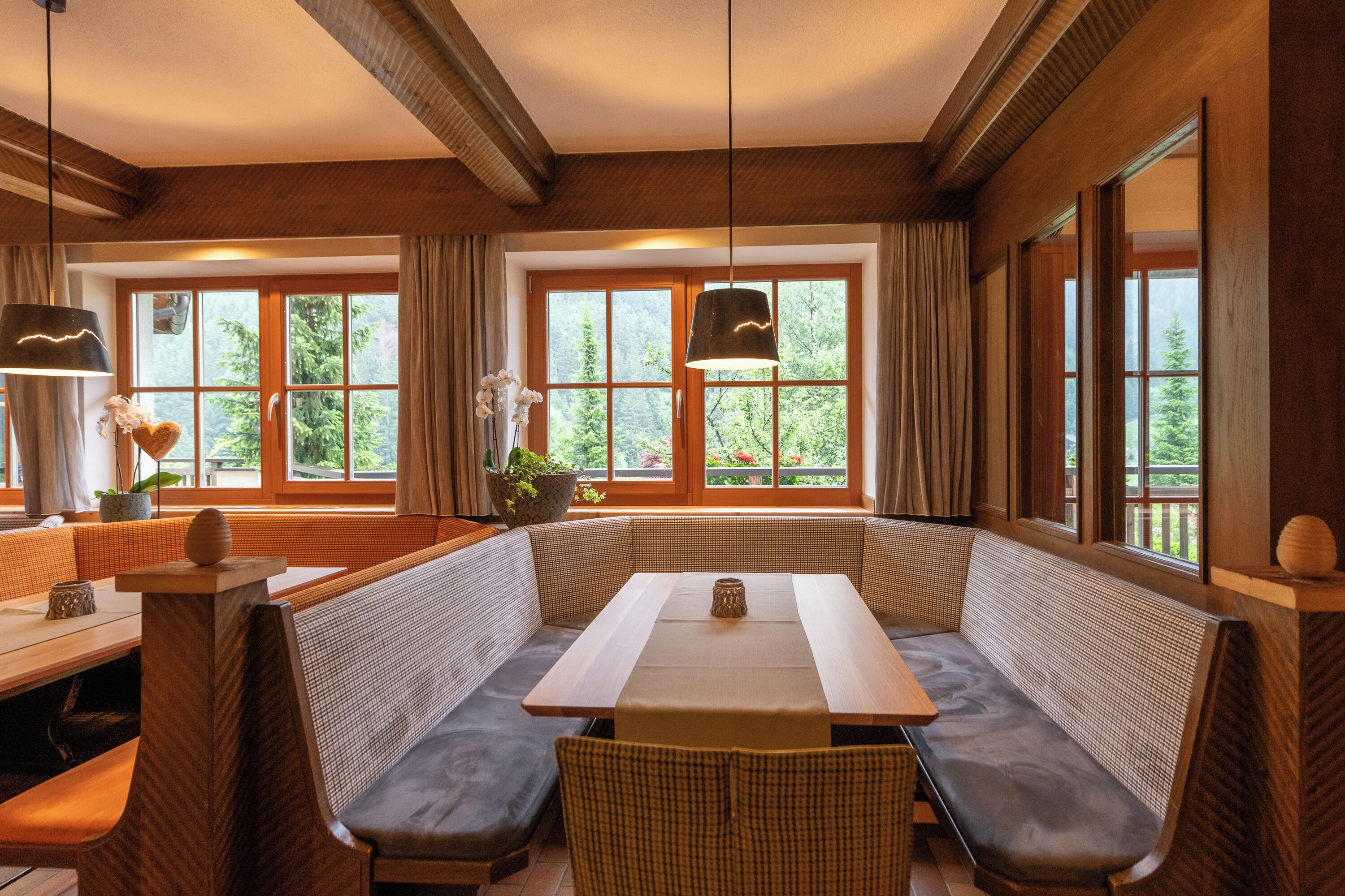 Una habitación acogedora con una zona de estar con banco de madera, una mesa y grandes ventanales con vistas a la vegetación.