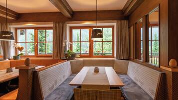 Una habitación acogedora con una zona de estar con banco de madera, una mesa y grandes ventanales con vistas a la vegetación.