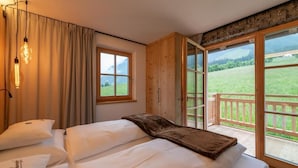 Ein Schlafzimmer mit zwei Betten, einem Fenster und einem Balkon mit Blick auf ein grünes Feld.
