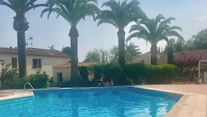 Kirkkaan sinisen veden uima-allas, jonka ympärillä on palmuja ja laatoitettu terassi.