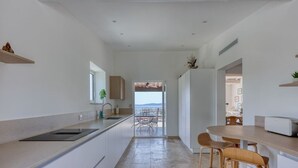 Una cocina moderna con vistas al mar, un área de comedor con mesa y sillas, y un refrigerador pequeño.