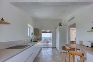 Eine moderne Küche mit Meerblick, ein Essbereich mit Tisch und Stühlen sowie ein kleiner Kühlschrank.