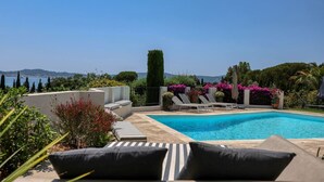 Un área de piscina con sillones, una piscina pequeña y vista al mar.