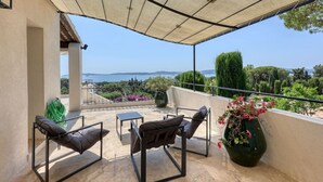 Un balcón con vista al mar, una mesa, dos sillas y una planta grande en maceta.