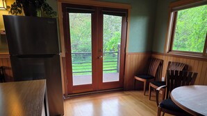 A kitchen with a refrigerator, a dining table with chairs, and a sliding glass door leading to a balcony. - Heron's Nest - Elegant King Master with custom woodwork, lofts and stained glass (Eugene)
