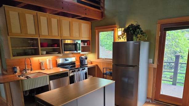 A modern kitchen with wooden cabinets, stainless steel appliances, and a large island. - Heron's Nest - Elegant King Master with custom woodwork, lofts and stained glass (Eugene)