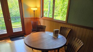 A round wooden table with a placemat and a menu stand, surrounded by wooden chairs with cushioned seats. - Heron's Nest - Elegant King Master with custom woodwork, lofts and stained glass (Eugene)