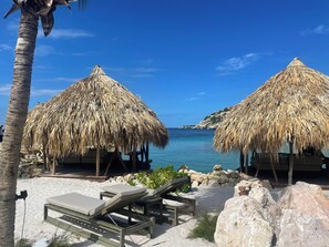 Un resort frente a la playa con construcciones de techo de paja, sillas de descanso y una vista despejada del mar.