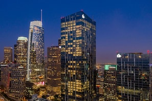 A cityscape at dusk with illuminated skyscrapers, including a prominent building with a clock tower and another with a green sign. - Luxury DTLA Skyline Residence (Los Angeles)