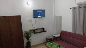 Een woonkamer met een bank, een klein tafeltje met planten, een aan de muur bevestigde televisie en een kledingkast.