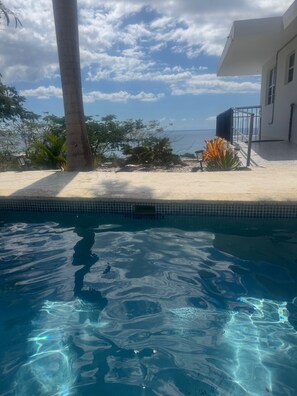 Una piscina con agua cristalina, rodeada de un patio con vistas al océano.