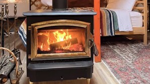 A yurt with a wood-burning stove, a bed, and a rug.