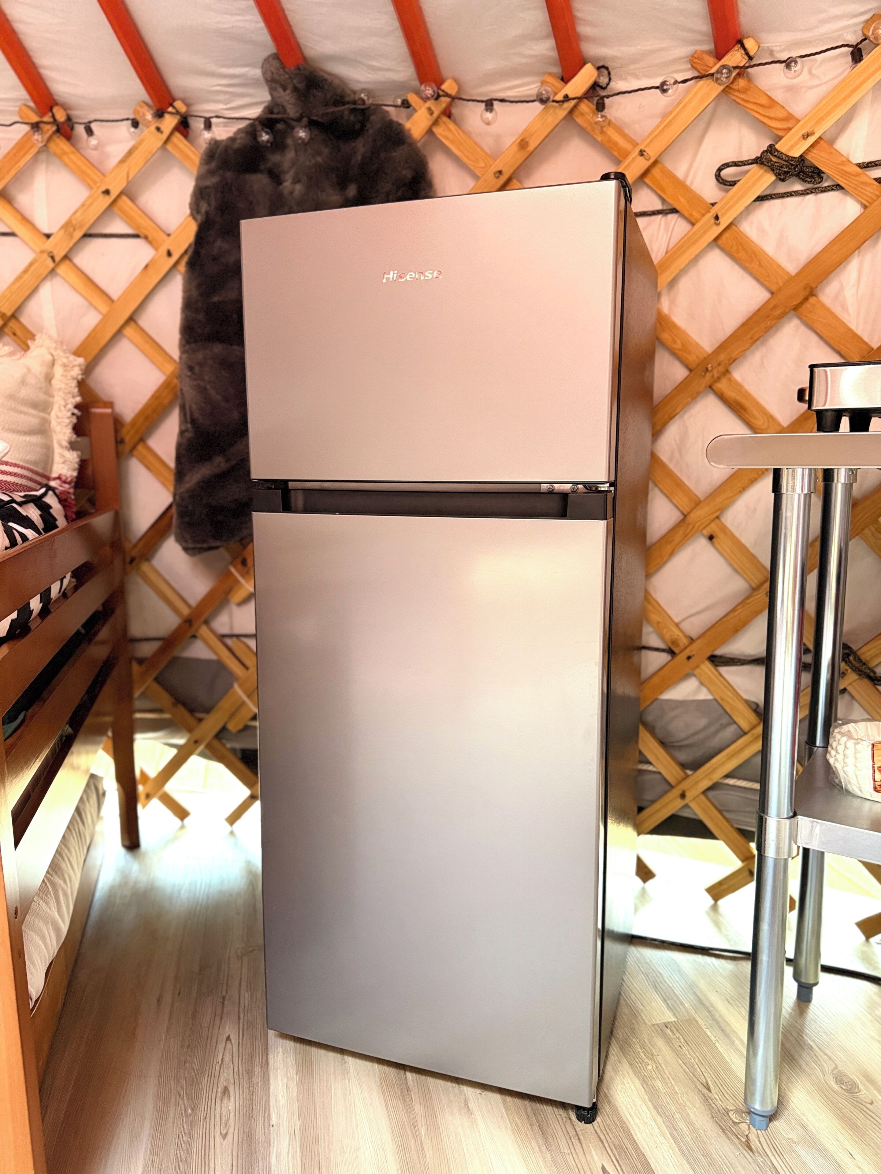 Un área de cocina compacta y moderna con un refrigerador de acero inoxidable, muebles de madera y una estructura similar a una tienda de campaña al fondo.