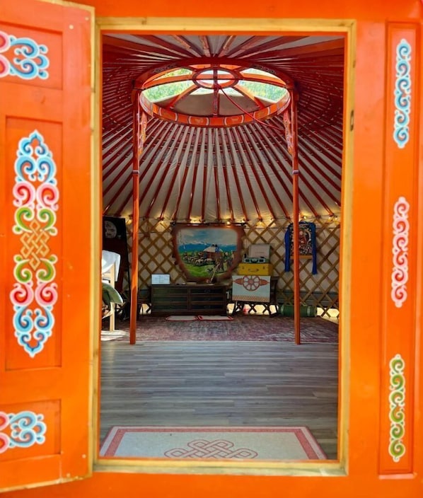 A traditional yurt with a wooden ceiling, a central painting, and a small table with items.