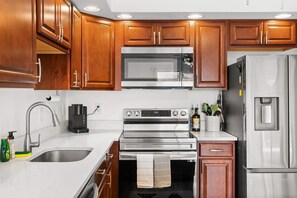 A kitchen with wooden cabinets, stainless steel appliances, a sink, and a coffee maker. - Family friendly waterfront escape- with a boat slip/short walk to beach (Ocean City)