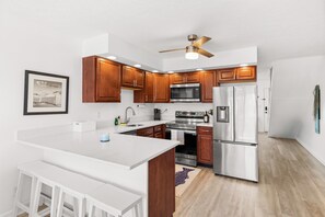A modern kitchen with wooden cabinets, stainless steel appliances, a ceiling fan, and a white countertop. - Family friendly waterfront escape- with a boat slip/short walk to beach (Ocean City)