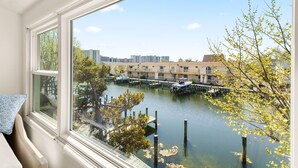 Uitzicht vanuit een raam op een jachthaven met aangemeerde boten, een heldere lucht en gebouwen op de achtergrond.