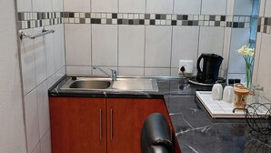 A compact kitchen with a sink, a coffee maker, and a small countertop with a vase of flowers.
