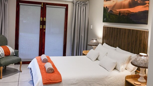 A hotel room with a bed, a chair, a nightstand, a lamp, a painting, and a window with curtains.