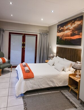 A hotel room with a bed, a chair, a nightstand, a lamp, a painting, and a window with curtains.