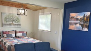 A bedroom with a blue sofa, a bed with a quilt, a painting of a tree, a window with blinds, and a blue wall. - Holly House in Sequim (Sequim)
