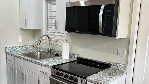 A kitchen with white cabinets, a stainless steel stove, a microwave, and a sink. - Holly House in Sequim (Sequim)