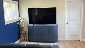 A living room with a dark blue sofa, a flat-screen TV on a cabinet, a door, and a window with blinds. - Holly House in Sequim (Sequim)