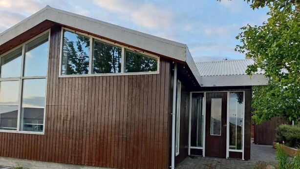 Ein modernes Gebäude mit großen Fenstern, einer Holzfassade und einem kleinen, angrenzenden Bauwerk mit Glastüren.