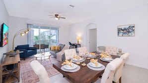 Uma sala de jantar com uma mesa de madeira posta para seis pessoas, um sofá azul e um ventilador de teto.